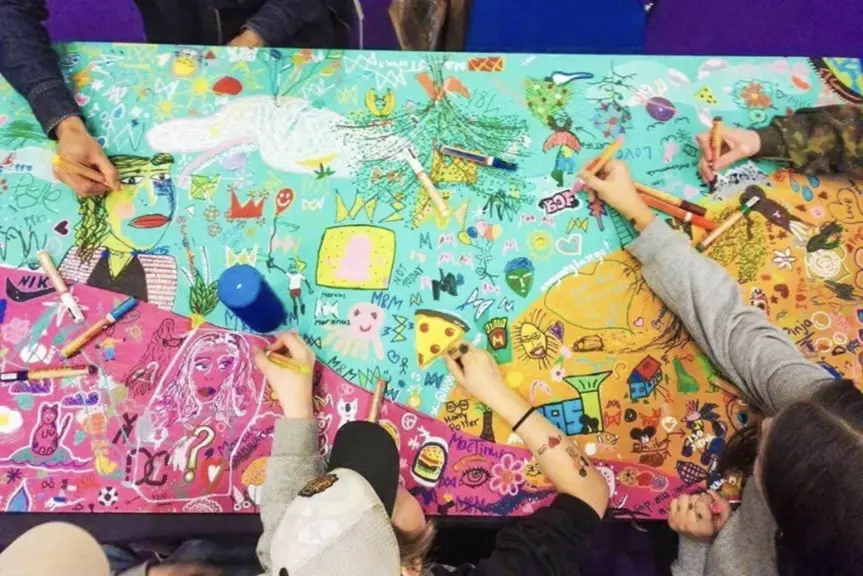 Children are drawing on a colourful tablecloth.