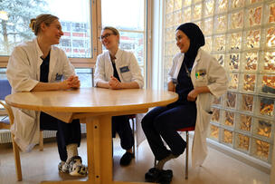 Erikoistuvat lääkärit Janita, Sofia ja Zahra istuvat pöydän ääressä ja juttelevat keskenään.