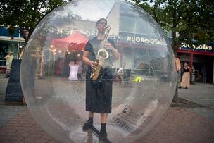 A woman playing saxophone inside a transparent plastic ball.