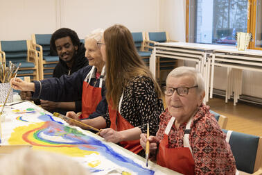 Two employees and two seniors paint a colourful artwork behind the table.