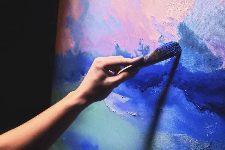 A person painting a work in shades of blue with a brush.