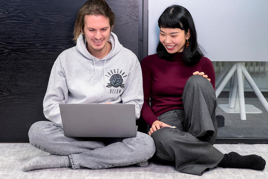 Two people are sitting on the floor and looking at a laptop.