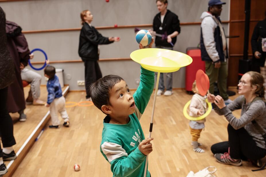 A child holding a stick in their hand and carefully placing a small ball on a plate on top of it.   