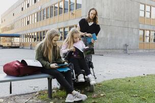 Kaksi oppilasta ja opettaja koulun pihalla.