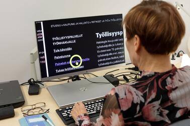 Nainen tutkii tietokoneen näytön suurennetulla tekstillä tietoa kaupungin työllisyyspalveluista. 