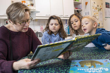 Aikuinen ja kolme lasta katsovat kirjaa.