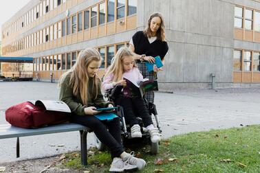 Kolme tyttöä koulutehtävien parissa ulkona välitunnilla.
