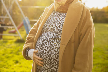 Odottava äiti seisoo pihalla ja pitää kättään vatsallaan.