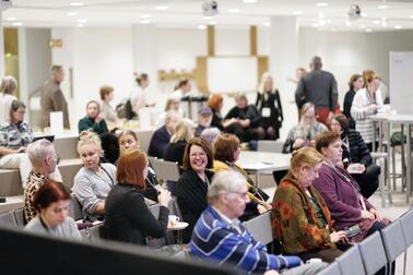 Representatives of organisations sitting side by side in the audience and talking to each other during an event. 