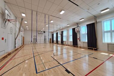 Ropes hanging from the ceiling and basketball hoops lining the walls in an empty, bright gym.