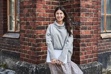 Nainen seisoo tiilirakennuksen edessä ja pitää käsissään kannettavaa tietokonetta, jonka kansi on suljettu.