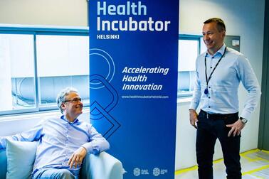 Two men next to the Health Incubator Helsinki roll-up.