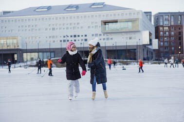 Kaksi nuorta henkilöä luistelemassa iloisina, toisella on kypärä päässä.