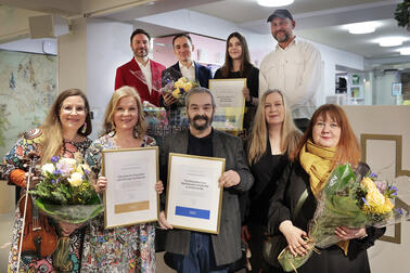 En grupp prisbelönta personer ler mot kameran medan de håller blommor och diplom i händerna.