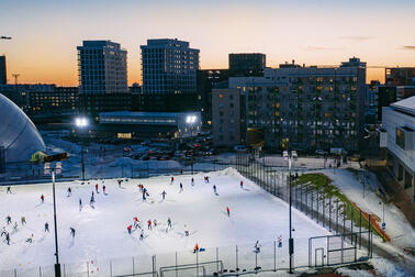 Människor åker skridskor och spelar ishockey på en upplyst isbana.