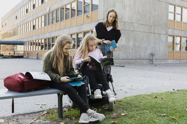 Kaksi oppilasta ja opettaja koulun pihalla.