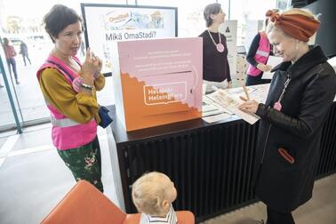 Ihmiset kohtaavat keskustellen OmaStadin merkeissä Helsingin keskustakirjasto Oodissa vuonna 2019.