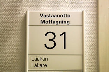 Seinällä oleva kyltti, jossa teksti "Vastaanotto Lääkäri". 
