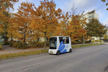 Robottibussi ajaa tiellä syksyisten puiden vierestä.