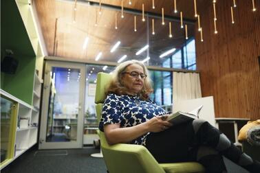 Nainen istuu nojatuolissa lukemassa kirjaa.