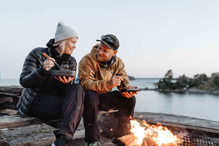 Nainen ja mies laavulla syömässä. Nainen ja mies laavulla syömässä.