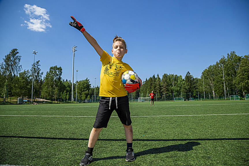 Lapsi tuulettaa jalkapallokentällä pallo kainalossaan. Lapsi tuulettaa jalkapallokentällä pallo kainalossaan.