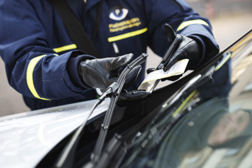 Pysäköinninvalvoja jättämässä pysäköintivirhemaksua auton tuulilasiin. Pysäköinninvalvoja jättämässä pysäköintivirhemaksua auton tuulilasiin.