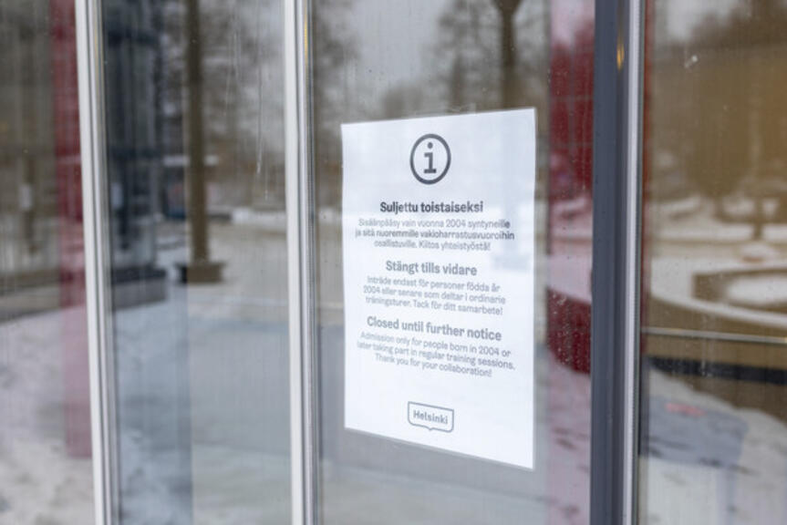 Koronarajoituksista kertova kyltti lasiovessa. Koronarajoituksista kertova kyltti lasiovessa.