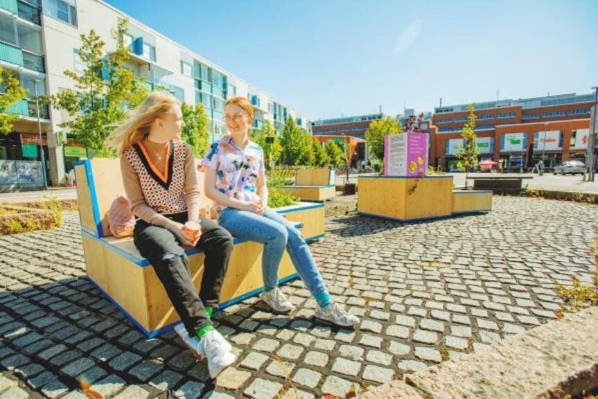 Kaksi tyttöä istuu Malmin torilla keidasmoduulin päällä Kaksi tyttöä istuu Malmin torilla keidasmoduulin päällä