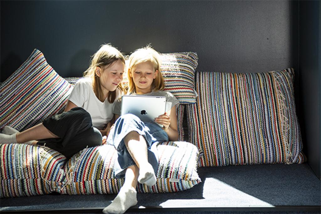 Kaksi koulutyttöä lukee yhdessä kannettavalta tietokoneelta Herttoniemen kirjastossa.