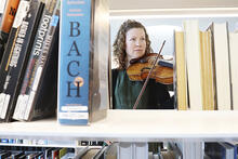 Nainen soittaa viulua kirjastossa hyllyjen välissä.