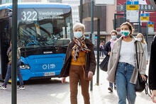 Kaksi naista maski kasvoillaan bussien laiturialueella.