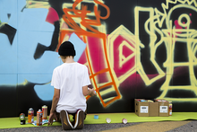 Nuori taiteilemassa graffitia seinään.