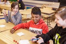 Kolme oppilasta koululuokassa pelaamassa arpakuutioilla.