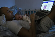 Isä ja vauva selaavat sängyssä verkkosivuja tietokoneella.