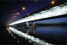 Lauttasaaren silta iltavalaistuksessa. Sillan valot heijastuvat meriveden pinnalle.