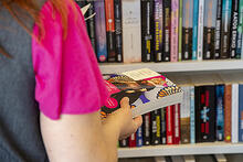 Nainen seisoo kirja kädessä kirjaston kirjahyllyn luona