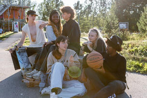 Kuvassa joukko nuoria istumassa ulkona aurinkoisena kesäpäivänä