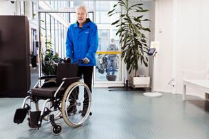 Mies työntämässä tyhjää pyörätuolia.