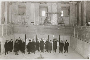 Mustavalkoisessa arkistokuvassa 1920-luvulta 16 miestä tummissa ulkovaatteissa uimahallin keskeneräisessä altaassa. Taustalla ylempänä mies työstää seinää.