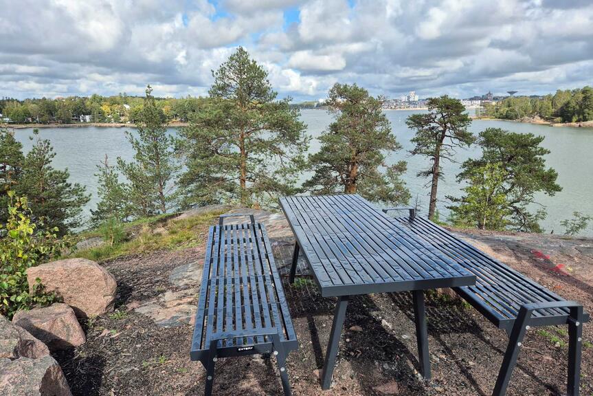 Pöytä ja tuolit kallioisessa metsämaisemassa.