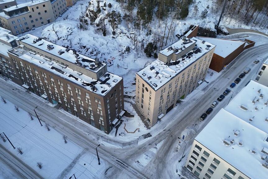 Ilmakuva Kruunuvuorenrannan asuinkortteleista talvisessa maisemassa. Rakennusten välissä näkyy kallioinen metsäalue ja katuverkko.