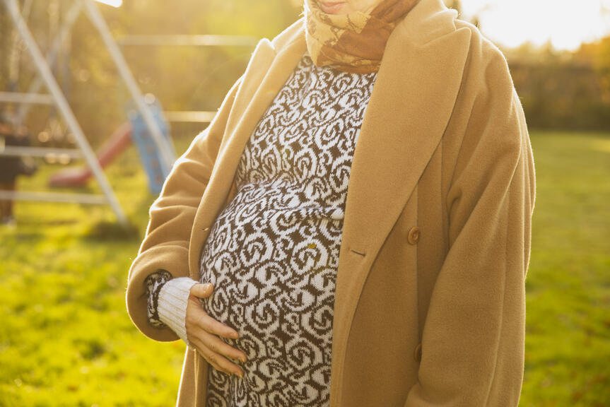 Odottava äiti seisoo pihalla ja pitää kättään vatsallaan.