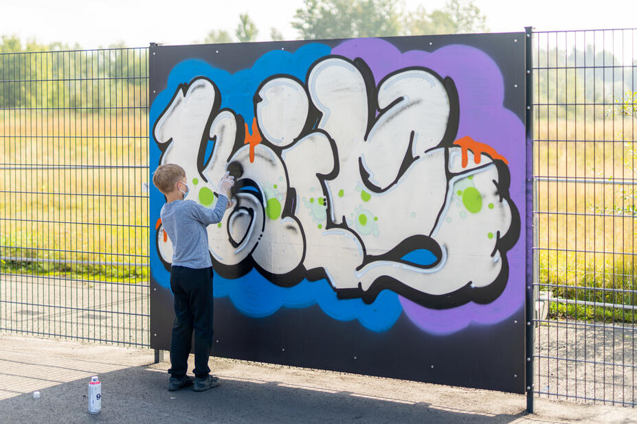 Poika maalaamassa graffitia graffitiseinään.