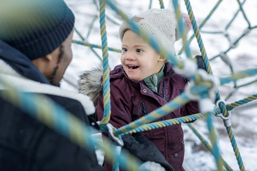 Mies ja lapsi katsovat hymyillen toisiaan leikkipuiston kiipeilytelineellä.
