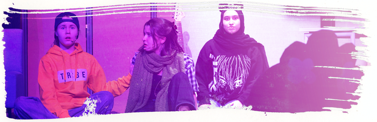 Kuvassa istuu kolme näyttelijää koulun esiintymislavalla.