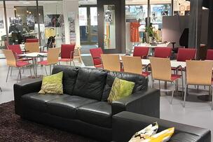 Yhteisötalo Alppilan olohuonemainen sisätila, jossa on mustat sohvat etualalla ja taka-alalalla kokouspöytäm, jonka ympärillä on punaisia tuoleja.