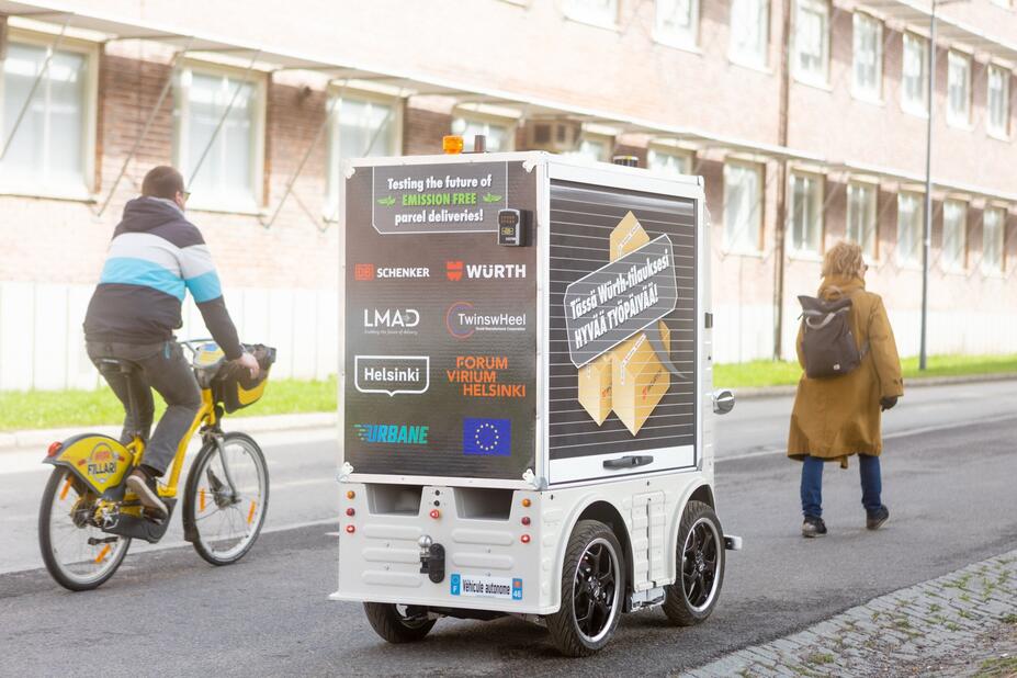 Pyöräilijä, jalankulkija ja pieni robottibussi kadulla.