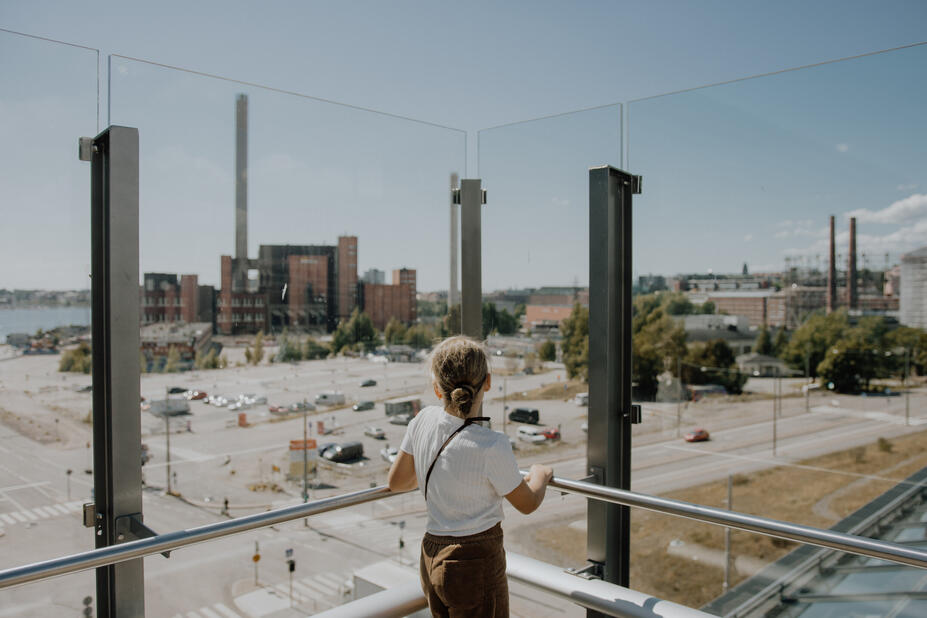 Nainen katselee parvekkeelta näkymää vanhalle tehdasrakennukselle.