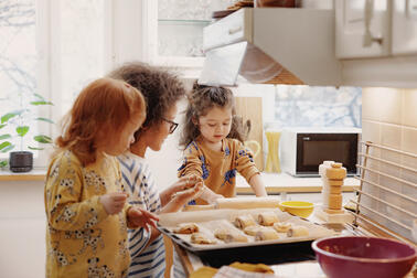 Kolme lasta osallistuu leipomiseen valoisassa keittiössä. 